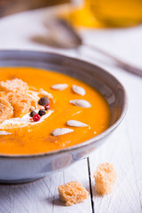 Delicious pumpkin soup in a bowl with croutons on white wood