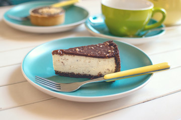 Salted Caramel Cheesecake on blue plate with fork, yellow tea pot and green cup. Delicious chocolate dessert and tea in cafe. Slice of tasty plain cheesecake