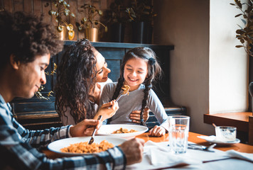 Happy african american family eating lunch together at restaurant and having fun - Powered by Adobe