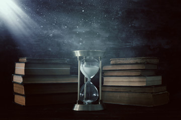 Hourglass as time passing concept and old books in front of black wall background. Conceptual photo...
