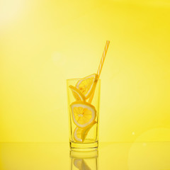 Glass with lemon in sunlight on yellow background