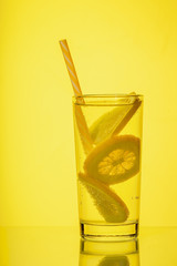 Full glass of fresh cool transparent water with lemon on yellow background