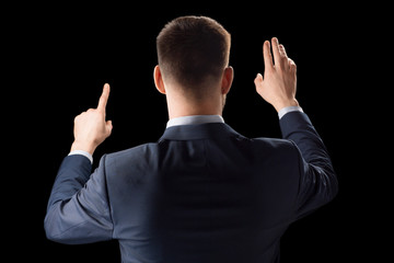 business, technology and augmented reality concept - businessman in suit working with invisible virtual screen over black background