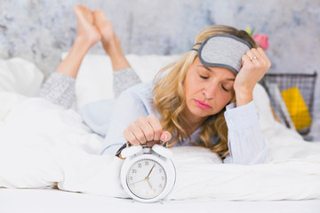blonde, pretty young woman doesn't like to get up in the morning and hates her ringing alarm clock...