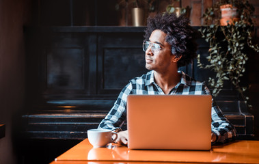 African man in glasses using laptop while sitting at restaurant, concept of young people working