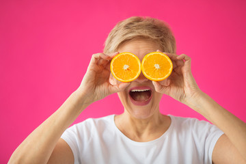 beautiful elderly woman in a white T-shirt with an orange in her hands on a pink background