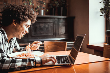 African american young man eating and working on laptop at restaurant