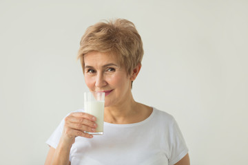 beautiful elderly woman in white T-shirt with a glass of milk on a white background