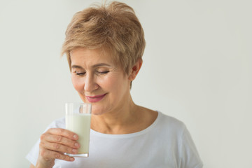 beautiful elderly woman in white T-shirt with a glass of milk on a white background