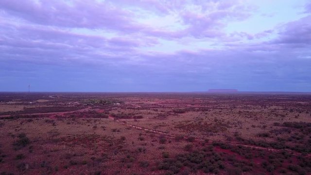 Contrast of a purple sky and a red earth in Australia's outback, with Uluru on the horizon.