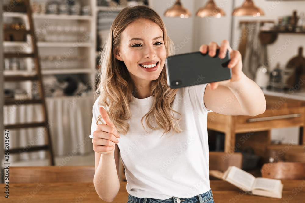 Sticker portrait of beautiful blond woman taking selfie photo on smartphone while standing in stylish wooden