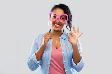 party props, photo booth and people concept - happy african american young woman with big glasses showing ok hand sign over grey background