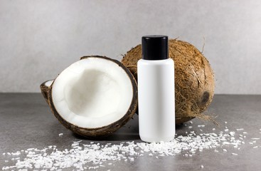 Coconut oil or natural cosmetics concept. Composition with white bottle mocap, coconuts and coconut flakes on a gray background.