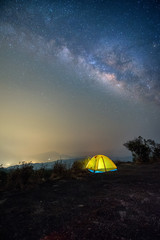 A yellow tent in the dark night background is the milky way and many stars on the sky.