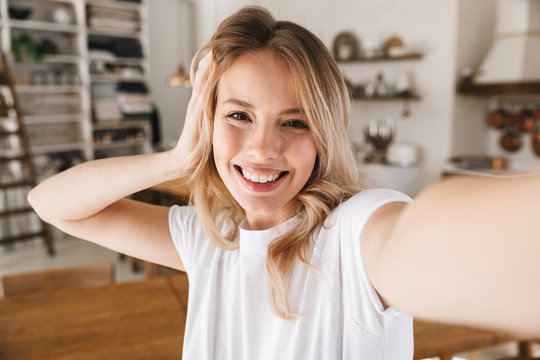 Image closeup of stylish blond woman laughing while taking selfie photo in living room