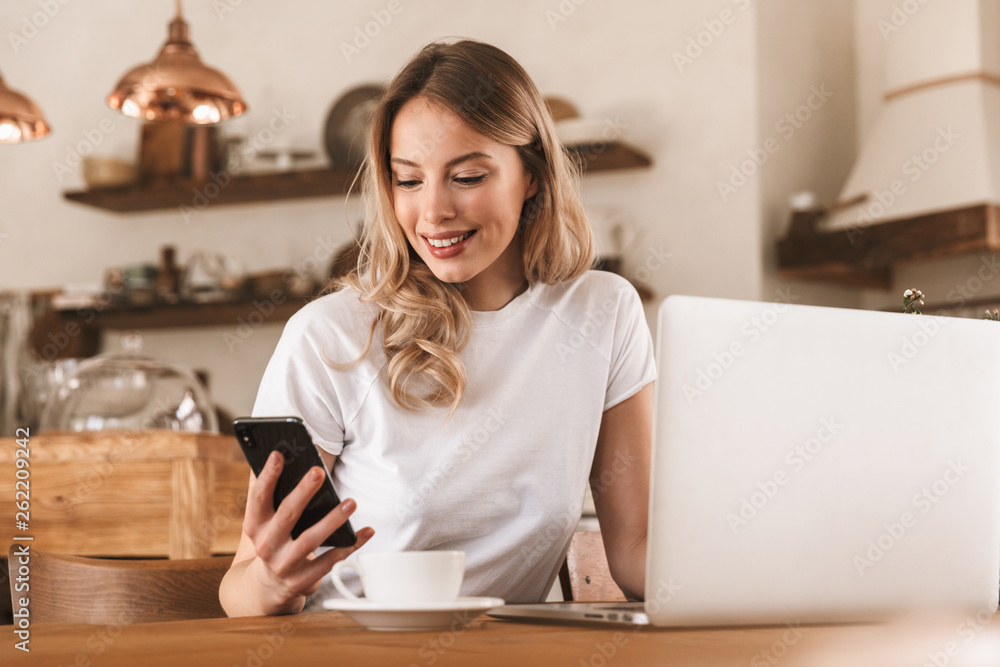 Poster portrait of attractive blond woman working on laptop and drinking coffee while sitting in cozy cafe 