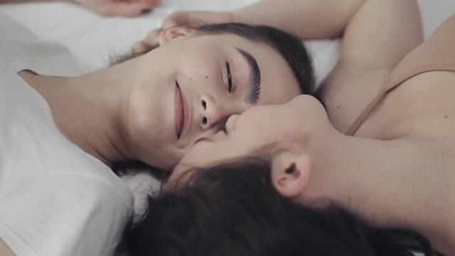 Happy lesbian girls are lying on the bed, smiling and enjoying each other. LGBT family concept, slow motion.