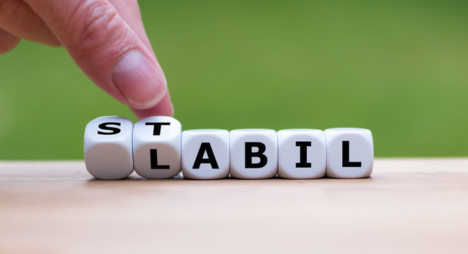 Stabil oder labil? Hand dreht einen W&uuml;rfel und &auml;ndert das Wort "Labil" in "Stabil" (oder umgekehrt).