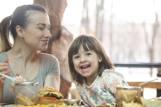 Mom With A Cute Daughter Eating Fast Food In A Cafe