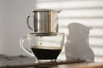 Fototapeta premium Coffee brewing on sunset. Traditional Vietnamese phin filtered coffee minimalist style.
