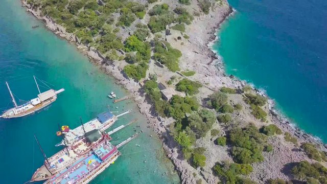 4K hd aerial top down drone shot over an island in aegean sea, boats at seaside, sunny weather, trees on the island, in Mugla Province, Turkey