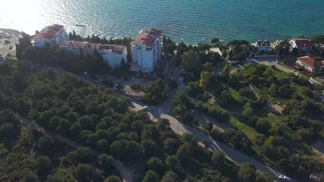 4k hd aerial drone shot over buildings and a car on the road, houses near sea, rays of sun reflecting on Aegean Sea, in Ilica Beach, Cesme, Izmir Province, Turkey