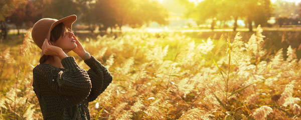 Beautiful young woman wearing knitted sweater and felt hat enjoying warm days in park