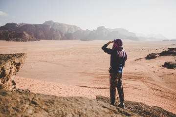 Fototapeta premium travel woman stay back to camera and looking from below hand near face on a dramatic Wadi Rum Jordanian desert world famous heritage touristic place scenic landscape location, mountain background