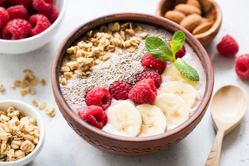 Superfood acai smoothie bowl with toppings such as banana slices, fresh raspberries, chia seeds and granola. Closeup view. Concept of clean eating, dieting, weight loss, vegan or vegetarian diet