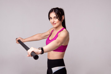 Beautiful muscular woman doing exercise with gymnastic stick on a gray background