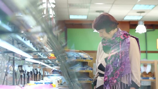 Elderly pretty woman shopping for fresh healthy food in the supermarket. Positive elderly woman consumer with bakery products in the food shop.