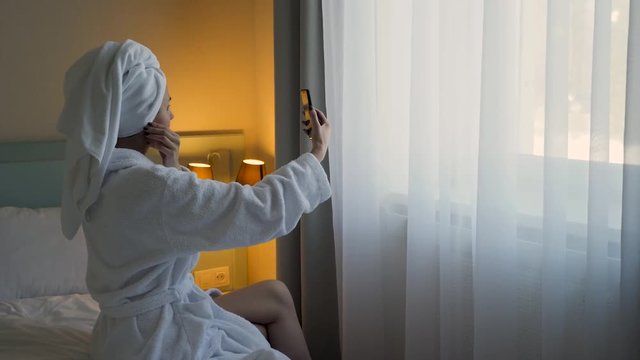 girl in a Bathrobe sits in front of the hotel window on the bed