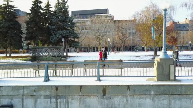 Cinematic drone / aerial footage moving sideways showing a pathway in Old Port (Vieaux Port) of Montreal with pedestrians walking, dry trees and buildings during winter season.