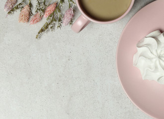 The granite background with pink cup of coffee, marshmallow on the the plate and flowers