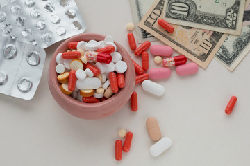 Assorted pharmaceutical pills in a bowl, empty blister packs and dollar bills on light background