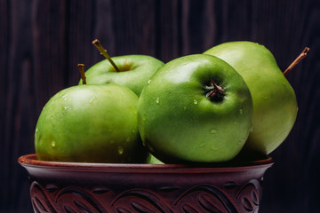 Ripe green apples close-up with dew in a bowl on a dark background