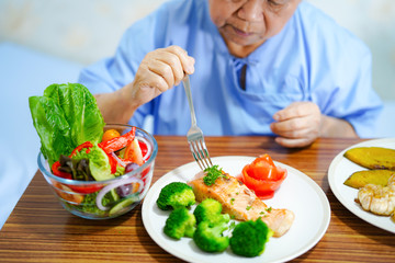Asian senior or elderly old lady woman patient eating breakfast healthy food with hope and happy while sitting and hungry on bed in hospital.