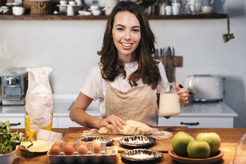 Cheerful young woman wearing apron preparing dough