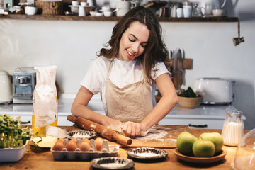 Cheerful young woman wearing apron preparing dough