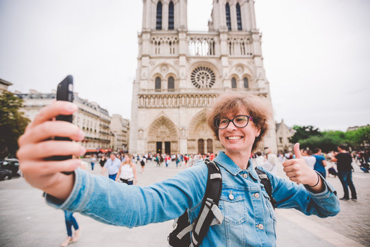 Tourist in Paris making funny selfie near Notre Dame Cathedral. Beautiful young Caucasian tourist woman with backpack in Paris making funny selfie hand holding phone, photo near Notre Dame Cathedral
