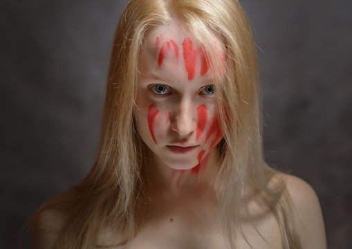 Portrait of young woman with paint on her face on dark background.