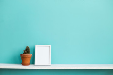 Modern room decoration with Picture frame mockup. White shelf against pastel turquoise wall with potted cactus plant.