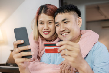 Asian couple use mobile shopping online with credit card together in living room at home.couple in home concept.