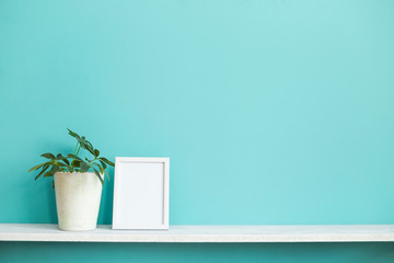 Modern room decoration with Picture frame mockup. White shelf against pastel turquoise wall with potted schefflera plant.