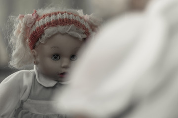 Creepy doll sits in front of a mirror. Doll with scary eyes looking at her reflection in the mirror