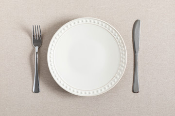 Empty plate, fork and knife on beige background linen tablecloth. Flat lay, top view, copy space 