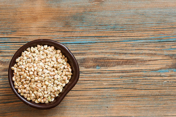 Buckwheat in a wooden bowl on an old wooden table, closeup view