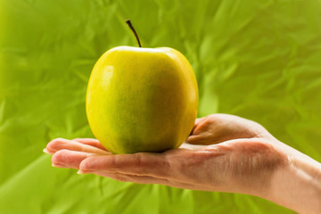 Yellow apple in hand on green background