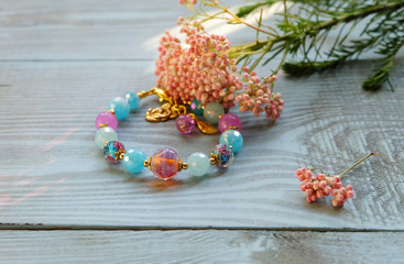 Bracelet with Murano glass and a yarrow flower on a blue wooden table. A beautiful composition with handmade jewelry.