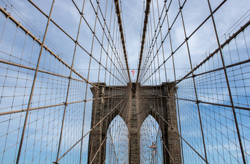The famous Brooklyn Bridge Bridge located in New York City in the United States of America showing the suspension wired and the USA flag at the top of the column on a part cloudy day with blue Skys.